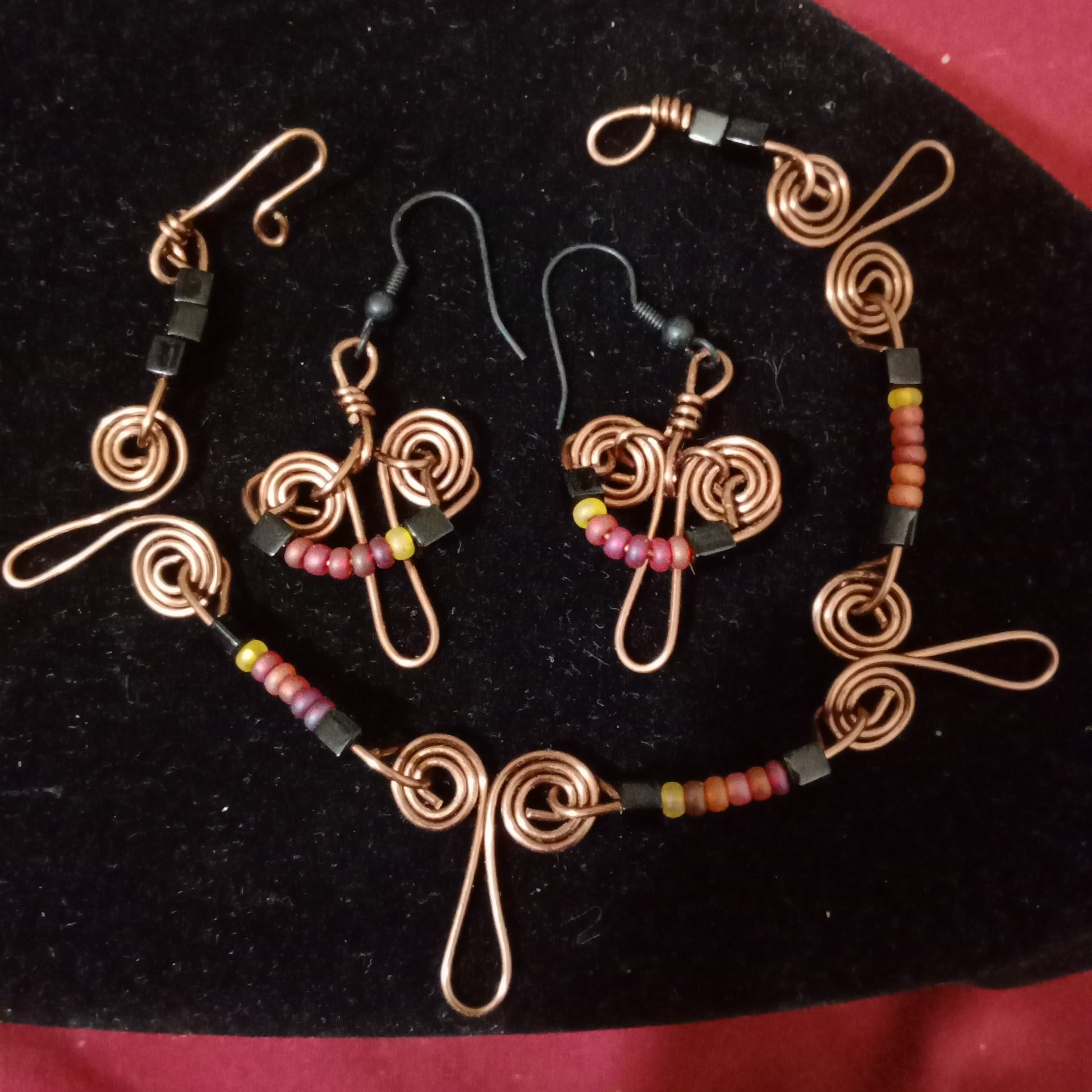 Wire beaded bracelet and earrings. Black, red and yellow beads. Brass double spiral wire pattern. Black hooks for earrings, hook and eye closure for bracelet